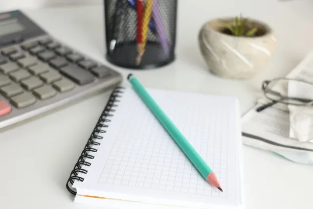 Calculadora, caderno, óculos e canetas sobre a mesa