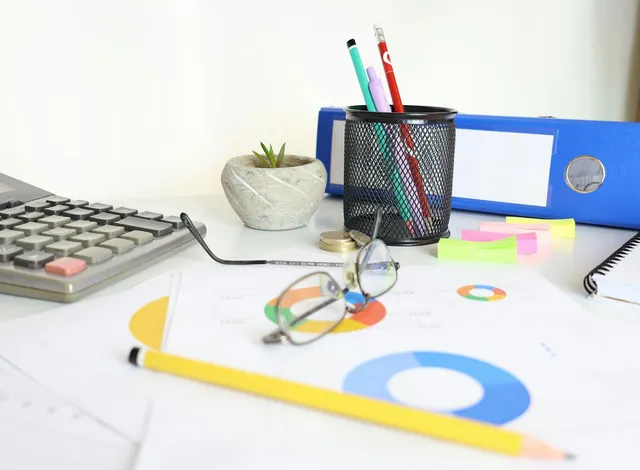 Calculadora, óculos e gráficos financeiros sobre a mesa